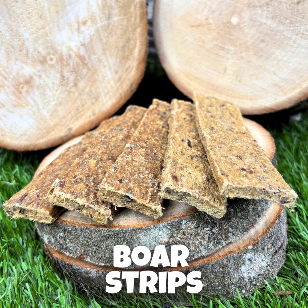 Natural dog treat – air-dried boar strips presented on wooden logs with a grass background