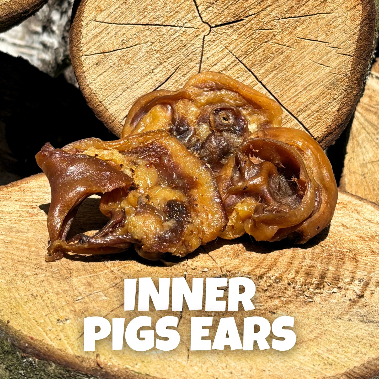 Natural dog treats – soft air-dried inner pig ears, displayed on rustic wooden logs. Protein-rich, grain-free chews perfect for gentle chewers.